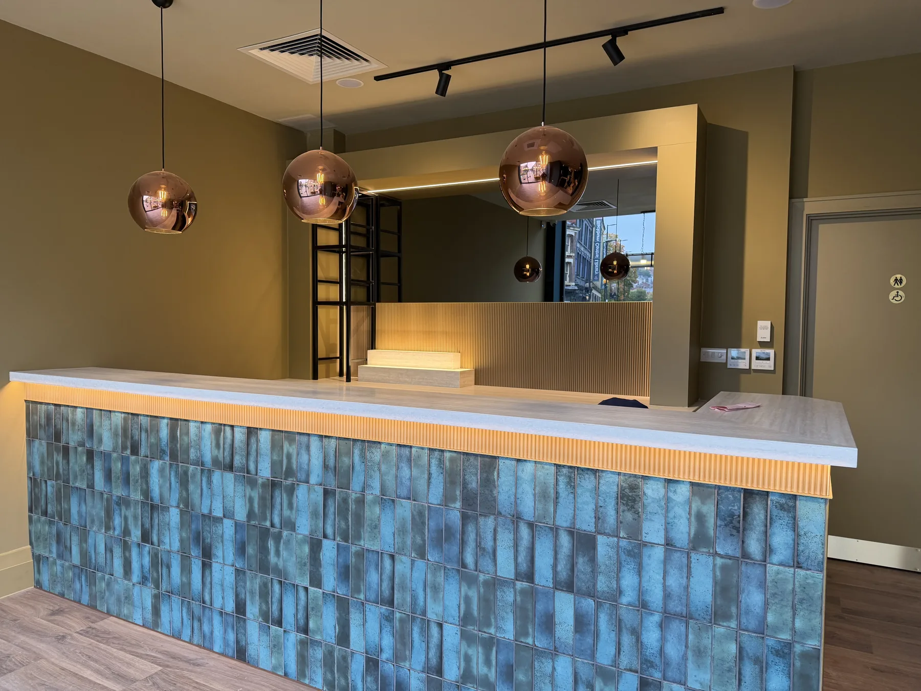 Bar with a blue glazed tile front, pale stone top and copper pendant lights