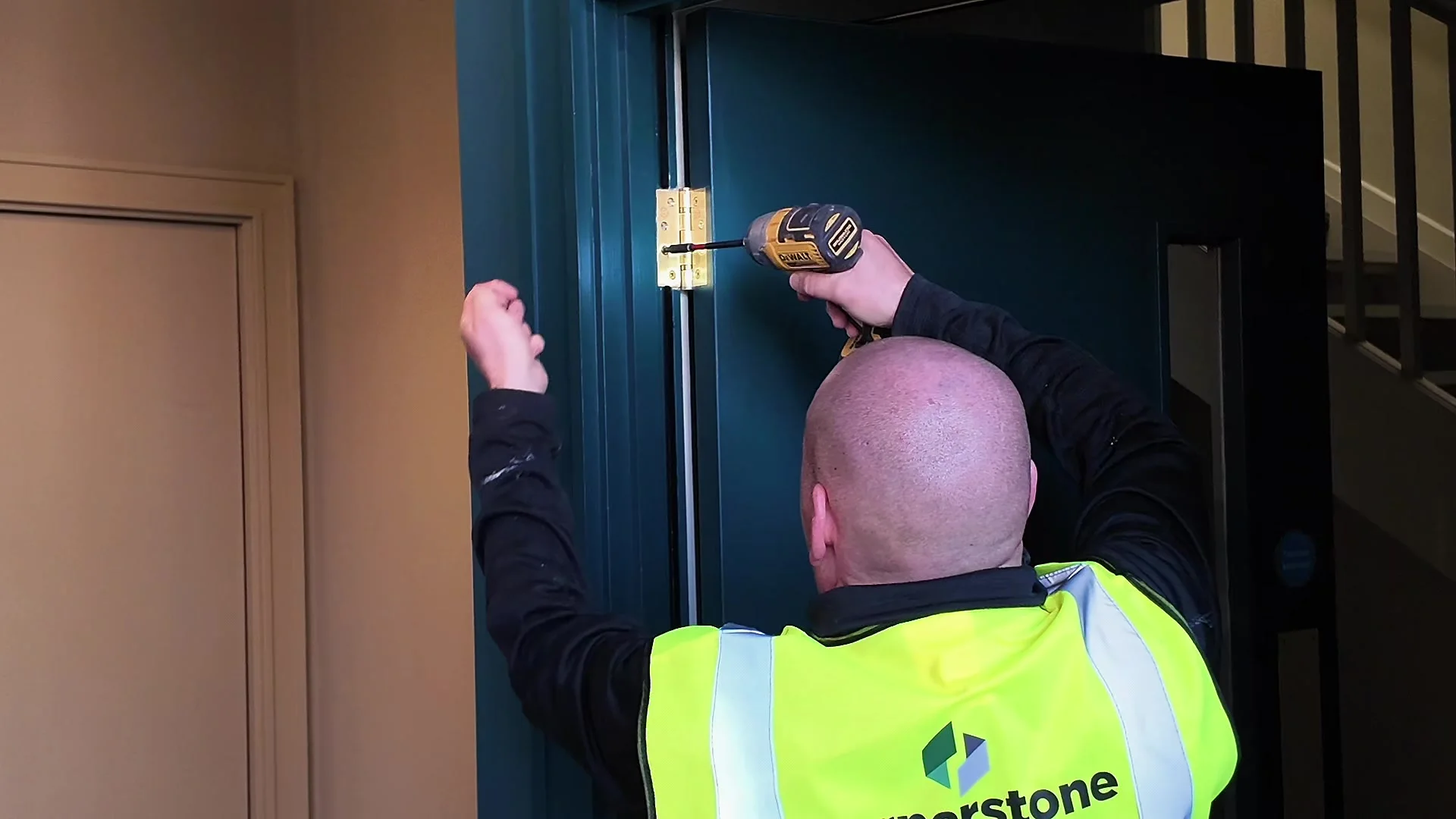 Cornerstone joiner in branded hi-vis fixing the hinges on a new fire door