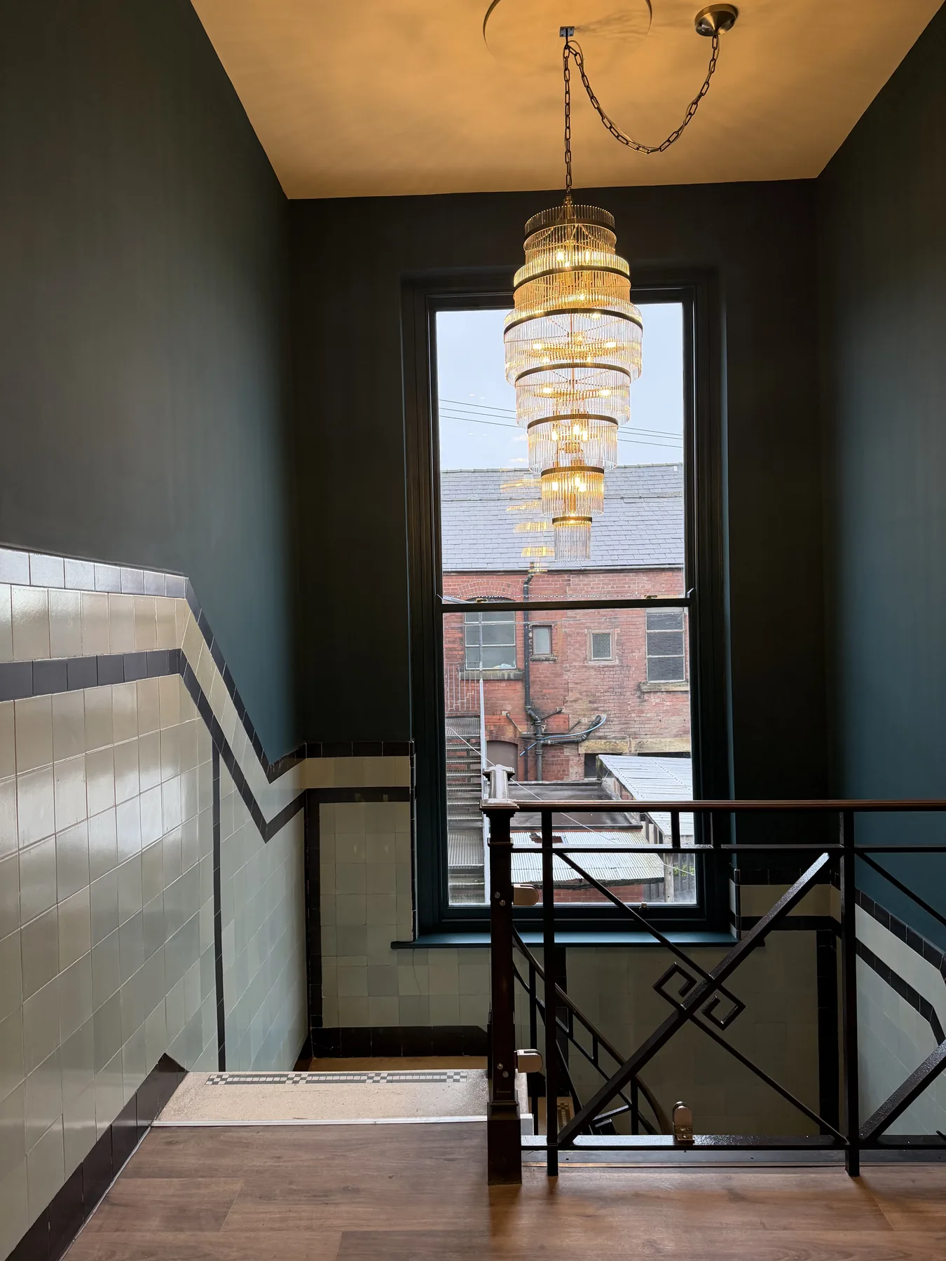 Staircase landing with a tiered crystal chandelier in front of a tall window
