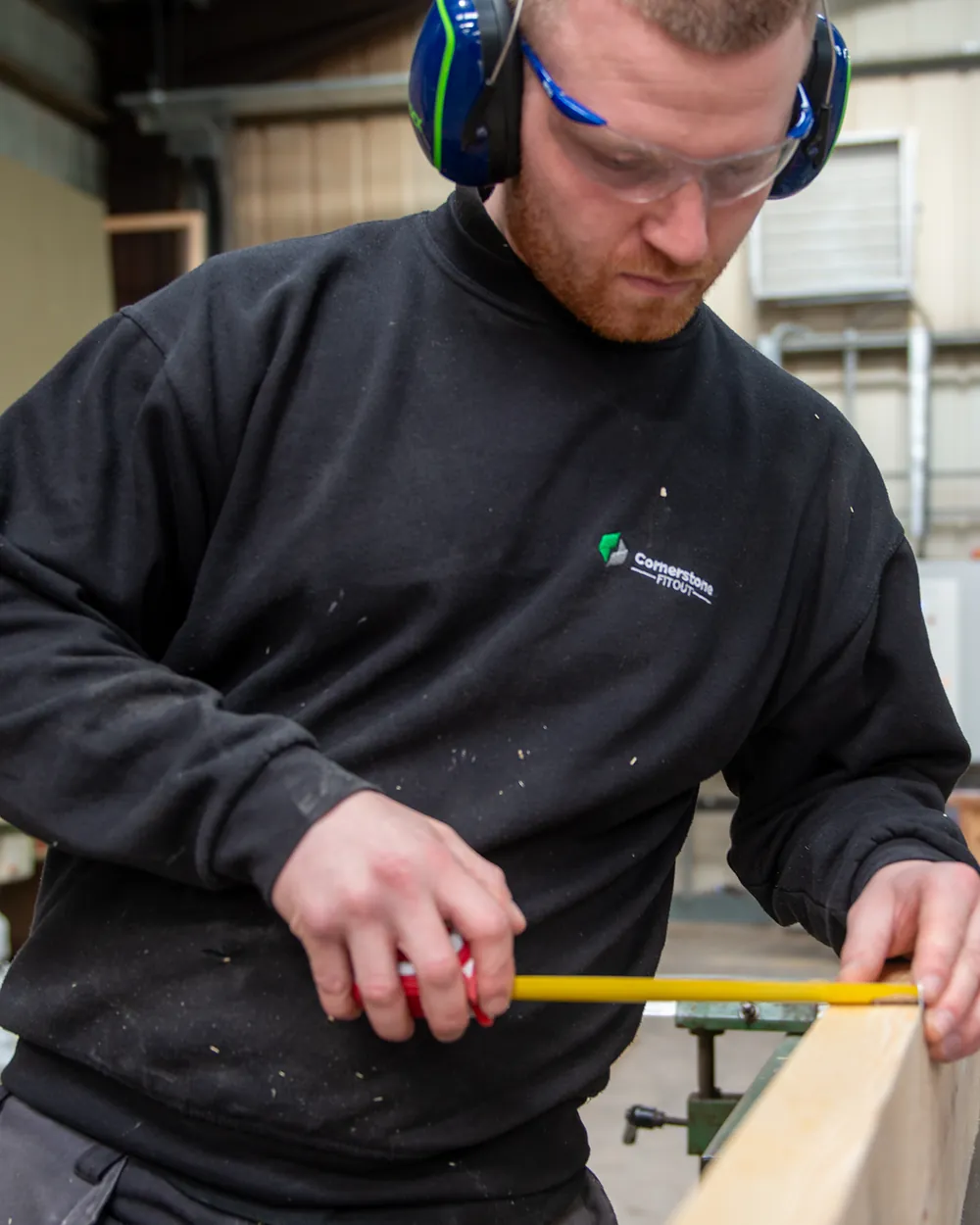 A Cornerstone joiner measuring timber in the workshop, wearing safety glasses and ear defenders