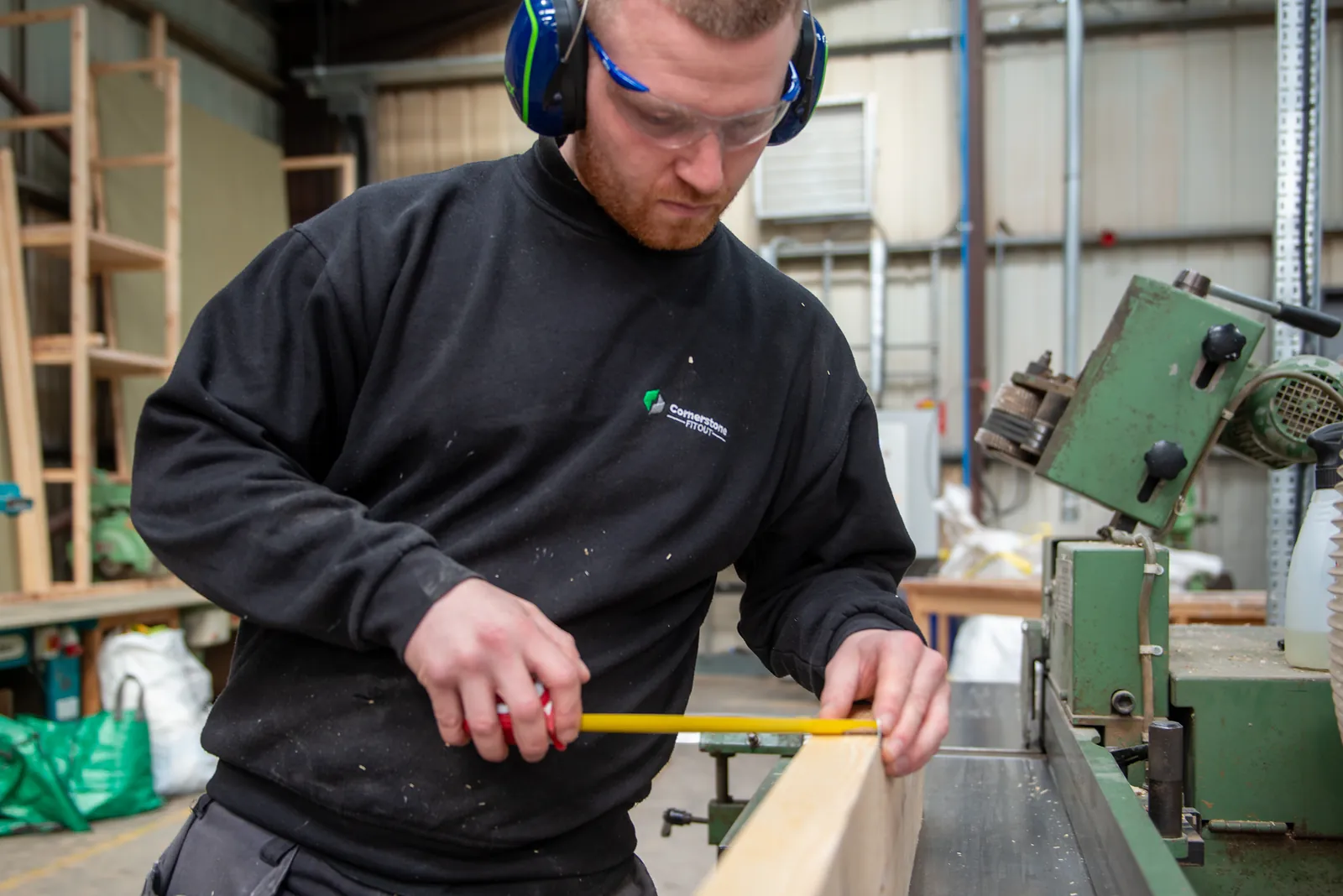 Cornerstone joiner in safety glasses and ear defenders measuring timber in our Lancashire workshop