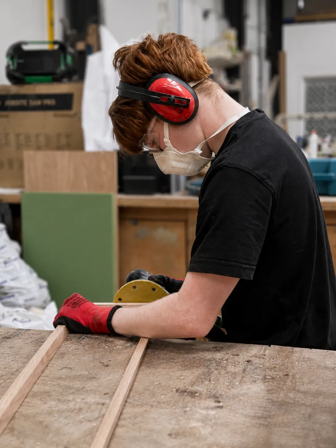 Apprentice sanding timber in full PPE