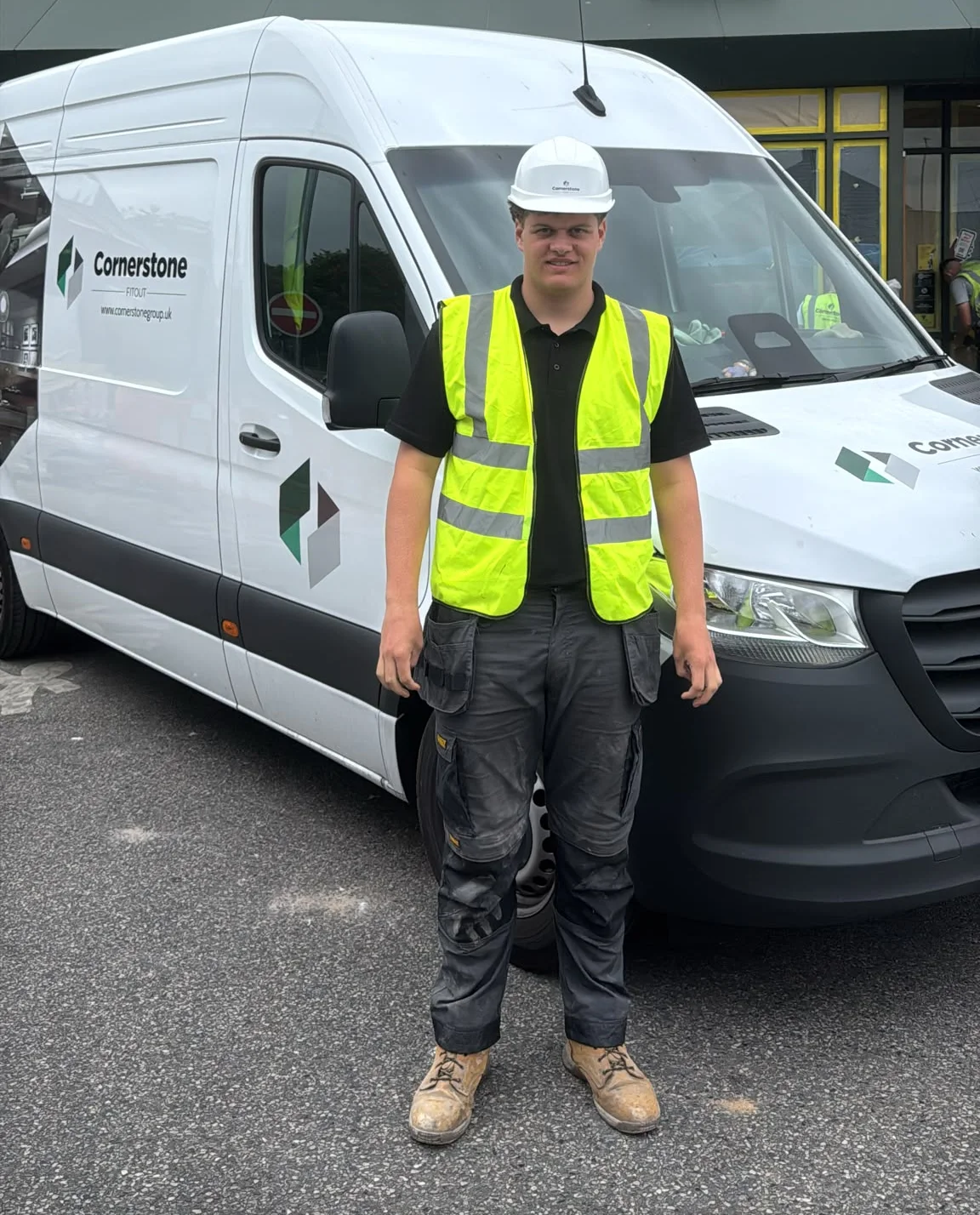 A Cornerstone apprentice in hard hat and branded hi-vis beside one of our vans