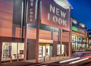 A New Look storefront in a retail park at dusk, lit up with a soft glow from signage and interior lights.